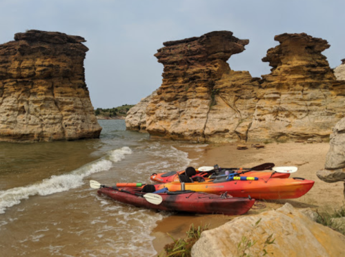 Colorful kayaks on a sandy beach near rocky cliffs, with gentle waves lapping at the shore.