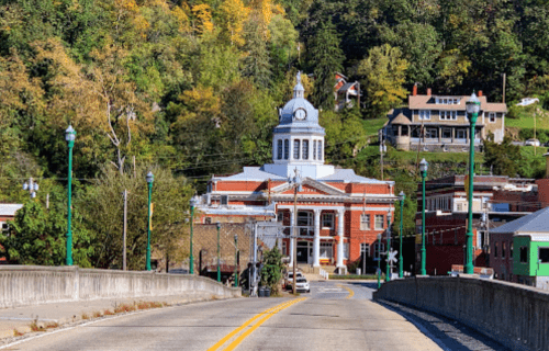 A view of a town hall with a clock tower, seen from a bridge, surrounded by trees and buildings in autumn colors.