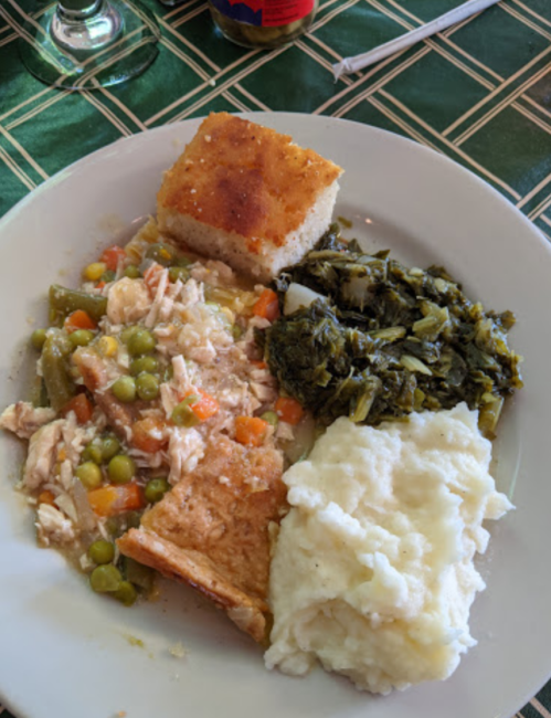 A plate of food featuring chicken, mixed vegetables, cornbread, collard greens, and creamy mashed potatoes.