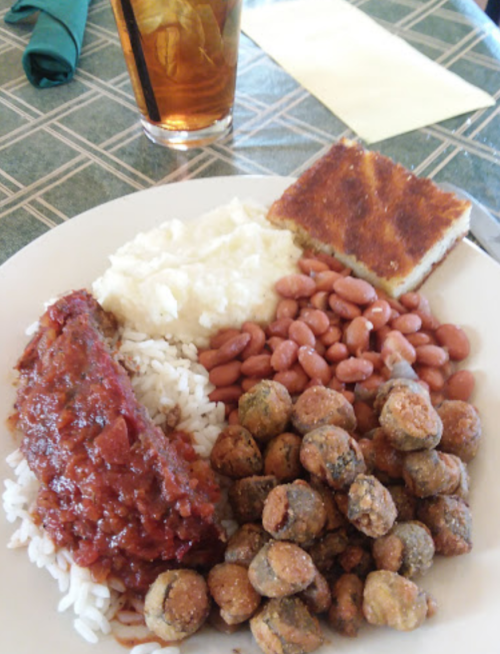 A plate of food featuring meatloaf, rice, mashed potatoes, pinto beans, fried okra, and cornbread, with a drink in the background.