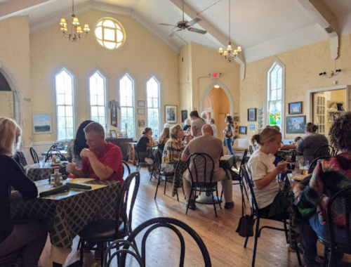 A busy restaurant interior with diners at tables, large windows, and artwork on the walls.