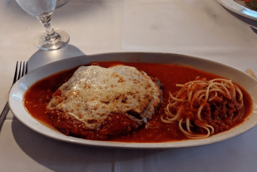 A plate of chicken parmesan topped with melted cheese, served with spaghetti and marinara sauce on the side.