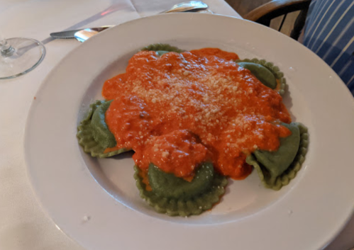 A plate of green ravioli topped with a rich red sauce and sprinkled with grated cheese.