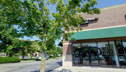 A storefront with a green awning, trees nearby, and a clear blue sky in the background.