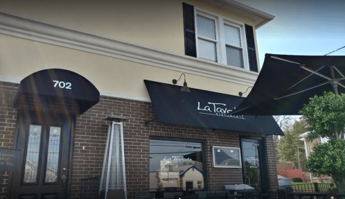 Exterior of La Tavola restaurant, featuring a black awning and a brick facade, with a door marked "702."