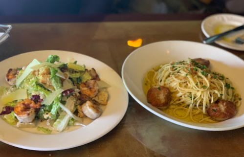 A plate of shrimp Caesar salad and a bowl of spaghetti with meatballs, garnished with herbs.