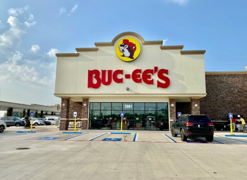 Exterior of a Buc-ee's store with a large sign, blue sky, and parking lot filled with cars.