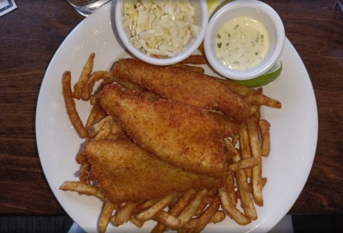 A plate of crispy fried fish fillets served with French fries, coleslaw, and dipping sauce.
