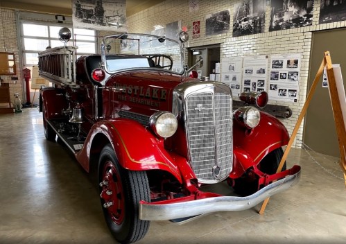 A vintage red fire truck displayed in a museum, with historical photos on the walls behind it.