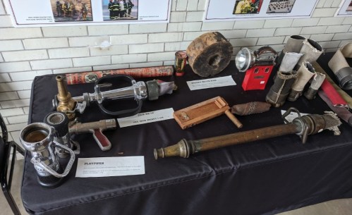 A display of various firefighting tools and equipment on a table, including hoses, nozzles, and a wooden tool.