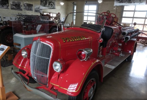 A vintage red fire truck with "PARMA" written on the front, displayed in a museum setting.