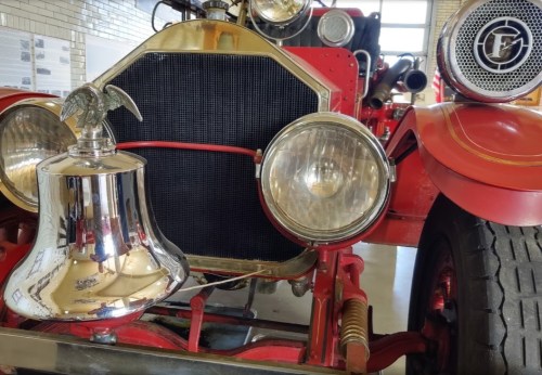 Close-up of a vintage red fire truck, featuring a shiny bell and large headlights.