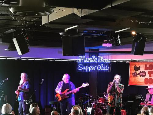 A live band performs on stage at the Music Box Supper Club, with colorful lighting and a lively atmosphere.