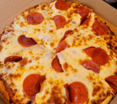 A pizza with melted cheese and pepperoni slices, cut into six pieces, in a cardboard box.