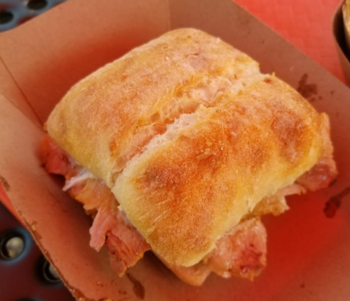 A freshly baked sandwich with a golden-brown crust, filled with layers of meat, served in a cardboard box.