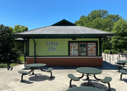 A green café building with outdoor seating, surrounded by trees on a sunny day. Sign reads "Pullen Café."