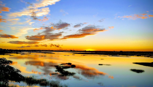 A serene sunset over a calm waterway, with vibrant orange and blue skies reflecting on the water's surface.