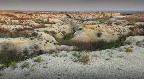 A panoramic view of a dry, rocky landscape with sparse vegetation and distant hills under a soft sky.