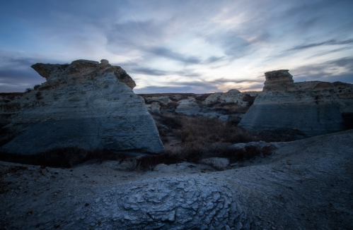 A dramatic landscape featuring unique rock formations under a cloudy sky at dusk.
