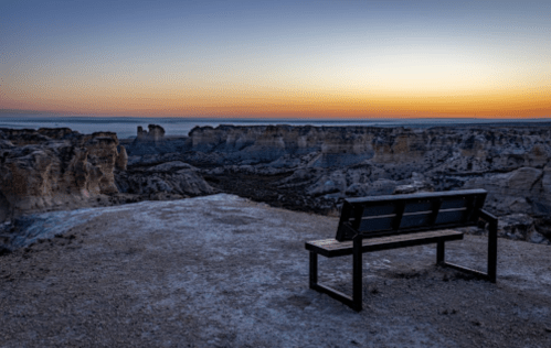 A solitary bench overlooks a vast canyon at sunset, with soft hues of orange and blue in the sky.