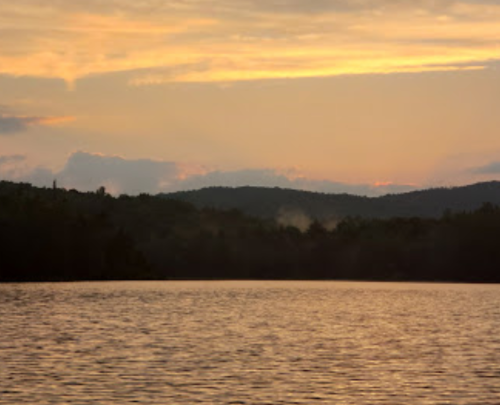 A serene lake at sunset, with gentle ripples and mountains silhouetted against a colorful sky.