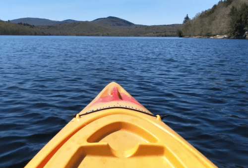 A yellow kayak on calm water, with mountains and trees in the background under a clear blue sky.