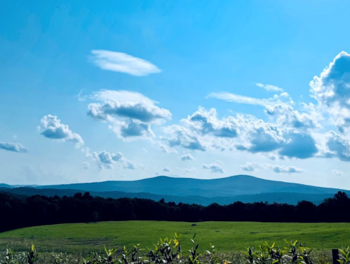 A scenic view of rolling hills under a bright blue sky with fluffy clouds and a green field in the foreground.