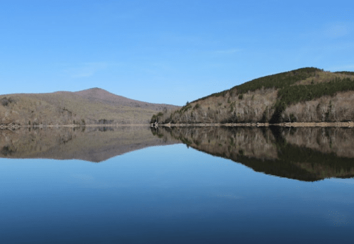 A serene lake reflecting a clear blue sky and surrounding hills, creating a peaceful natural landscape.