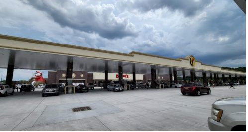 A large gas station with a convenience store, featuring a red cartoon character and cloudy skies above.