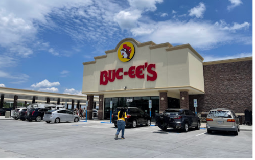 A person walks towards a Buc-ee's store with a blue sky and clouds in the background.