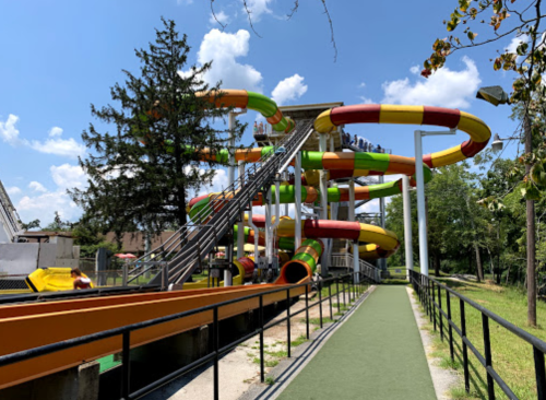 Colorful water slides twist and turn at a water park, with a clear blue sky and trees in the background.
