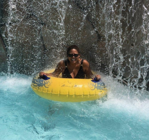 A person in a yellow inner tube smiles while enjoying a water slide under a waterfall.