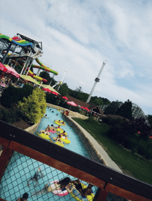 A water park scene with a lazy river, colorful slides, and people enjoying the attractions under a cloudy sky.