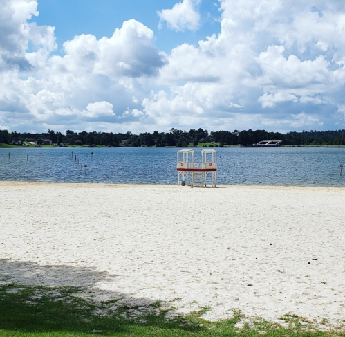 A sandy beach with a lifeguard tower overlooking a calm lake under a partly cloudy sky.