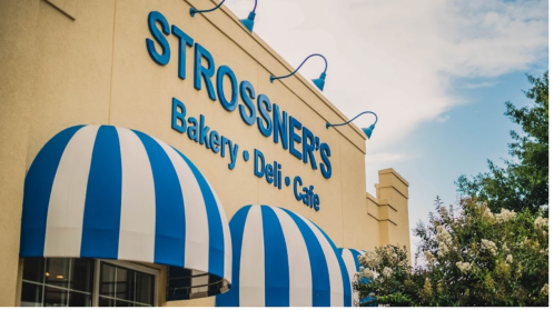 Sign for Strossner's Bakery Deli Cafe with blue and white striped awnings under a clear sky.