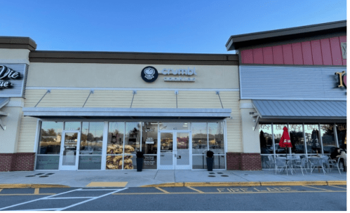 Exterior of a cookie shop with large windows, displaying baked goods, located in a shopping plaza.