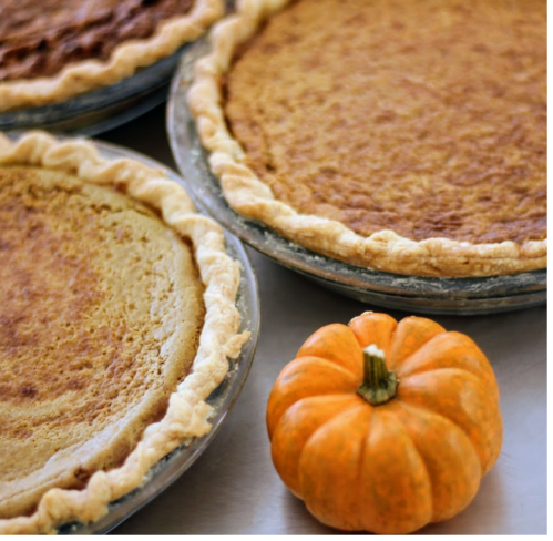 Three pumpkin pies in metal pans with a small orange pumpkin in front.