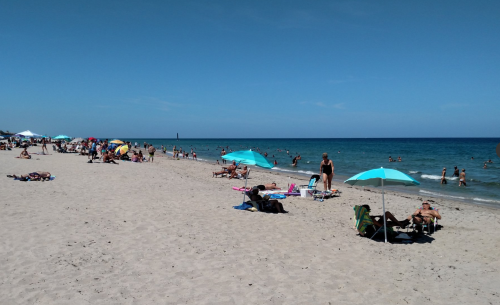 A sunny beach scene with people relaxing on the sand, swimming in the water, and colorful umbrellas dotting the shore.