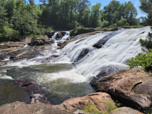 A serene waterfall cascading over rocky terrain, surrounded by lush green trees under a clear blue sky.