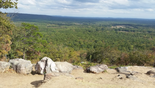 A panoramic view of a lush green valley from a rocky overlook under a partly cloudy sky.