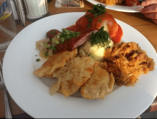 A plate of assorted dishes including dumplings, sauerkraut, mashed potatoes, and sliced meat, garnished with herbs.
