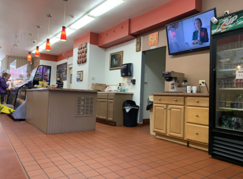 Interior of a casual eatery with a counter, TV, and seating area; customers are visible in the background.