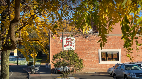 A brick bakery building surrounded by autumn leaves, with a sign partially visible in the background.