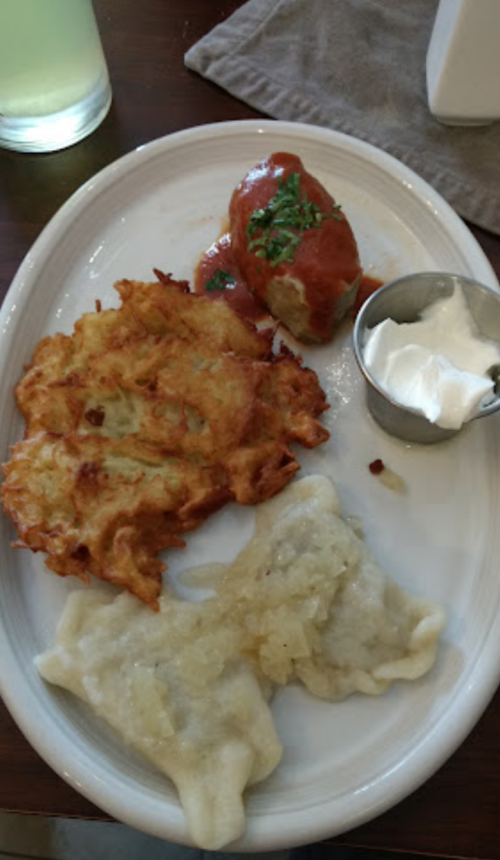 A plate with potato pancakes, stuffed cabbage in sauce, and dumplings with a side of sour cream.