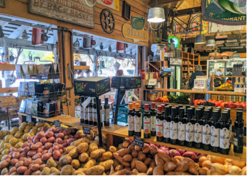A vibrant market display with various potatoes and bottles of oil on wooden tables, surrounded by rustic decor.