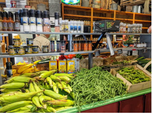 A vibrant market display featuring fresh vegetables, spices, and condiments, including corn, green beans, and peppers.