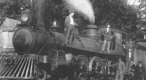 A historic black and white photo of a steam locomotive with men standing on and around it.