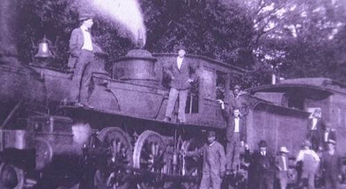 Black and white photo of a steam locomotive with several men posing on and around it.