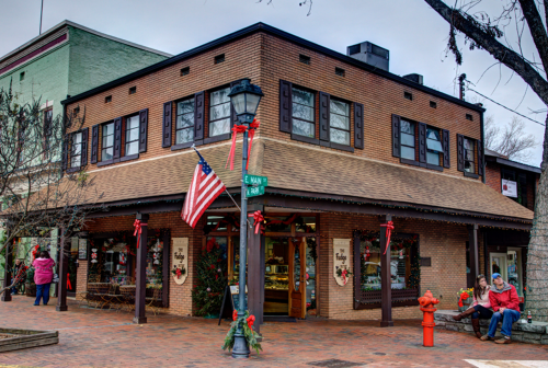 A festive storefront decorated for the holidays, with an American flag and people enjoying the scene outside.
