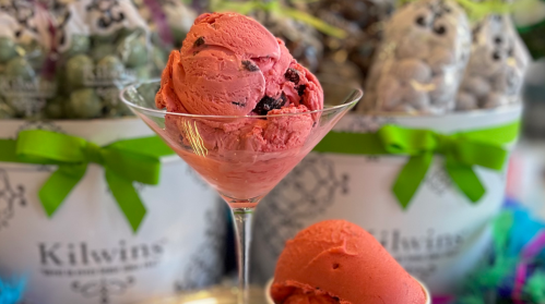 A scoop of vibrant pink ice cream in a martini glass, with colorful candy bags in the background.